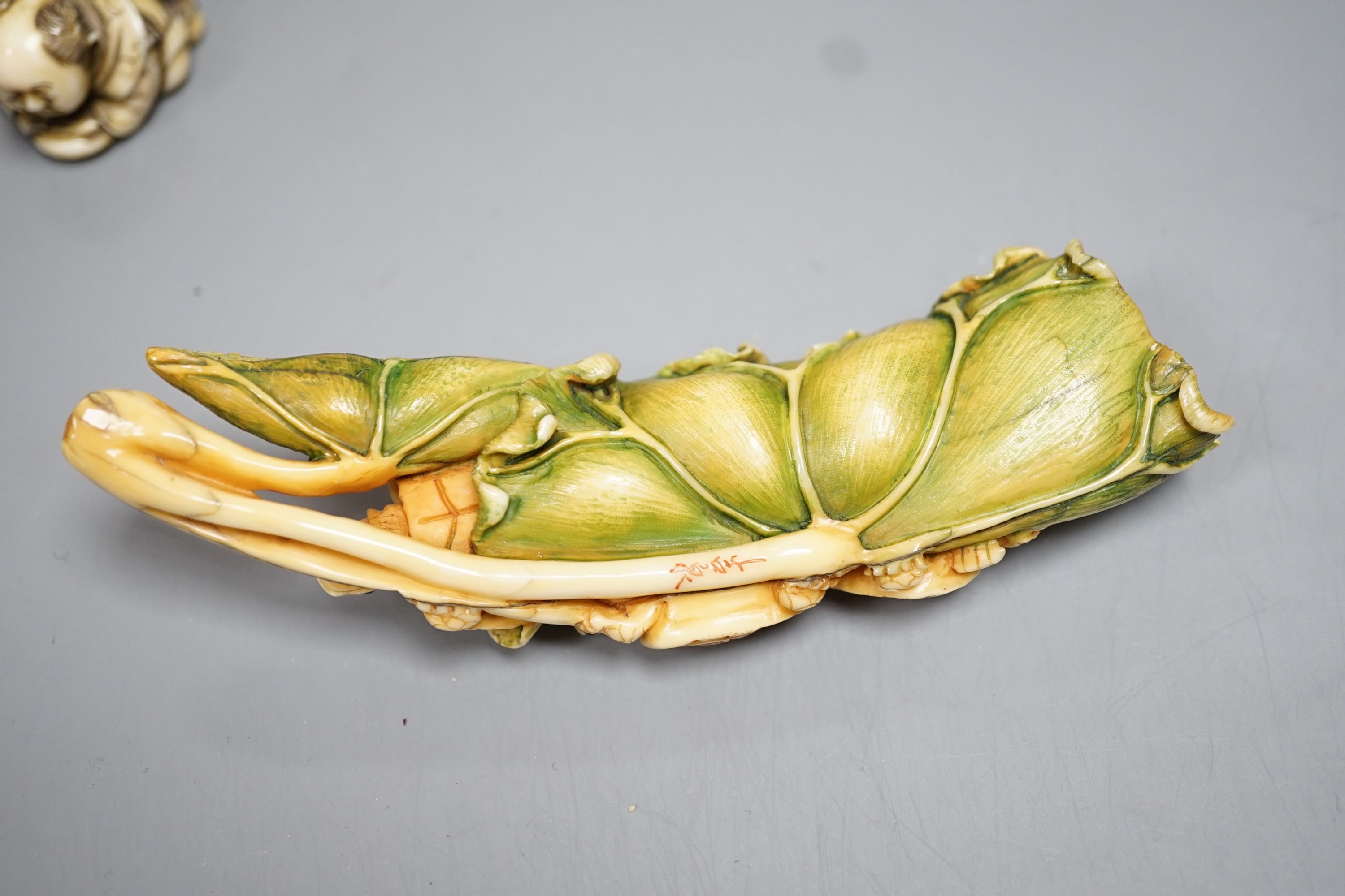 A Japanese ivory Netsuke of two boys holding a noh mask, an ivory Netsuke in the form of three animal heads and a coloured Ivory carving of tortoises on a lotus leaf, all singed (3) largest 12cm